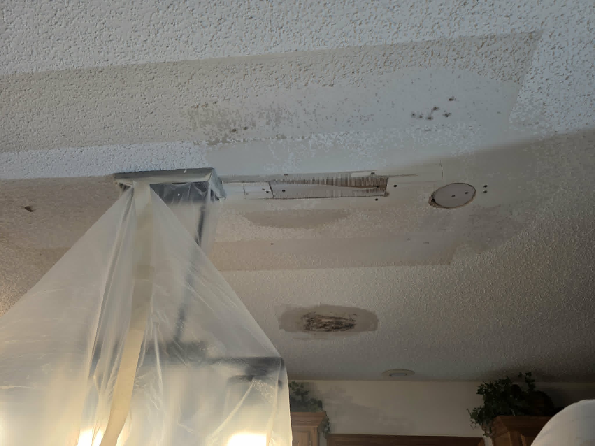 Kitchen ceiling opened up mid-repair with plastic sheeting protecting the room